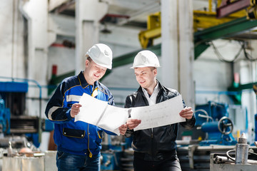 A young successful engineer discusses technical documentation with his help in the territory of a modern plant