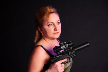 A middle aged, white, woman holds a semi automatic pistol with silencer and collimator against black