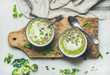 Spring detox broccoli green cream soup with mint and coconut cream in bowls on rustic wooden board over marble background, top view. Clean eating, dieting, vegan, vegetarian, healthy food concept