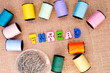 Sewing - Thread spelt in buttons with cotton reels on burlap background
