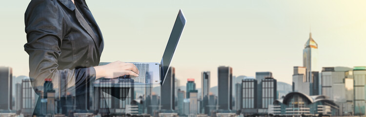 Aufkleber - Businesswoman typing on laptop computer double exposure with blur cityscape building in morning,Business banner size,Technology communication concept