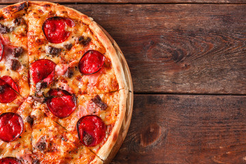 Delicious fresh pizza with salami, ham, cheese, meat and bacon served on wooden rustic table, flat lay. Dark background with free space. Italian traditional cuisine.