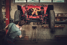 Mechanic Working On Classic Car Wheels And Suspension In Restoration Workshop
