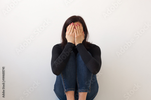 Cuadros en Lienzo A girl in black clothes sits alone by the white wall