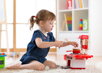 Pretty kid girl playing with a toy kitchen in children room