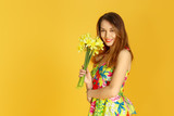 Fototapeta Tulipany - Young woman against yellow wall with flowers in hand