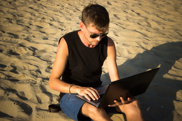 Young man are working on laptop computer on the beach. Downshifting and freelance concept.