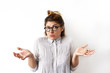 © shurkin_son - Indoor shot of emotional funny young woman in eyeglasses and formal shirt looking confused and puzzled, her arms out shrugs shoulders. Emotions, facial expressions, feelings, body language
