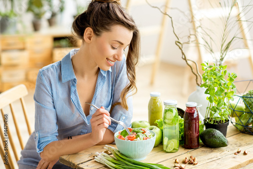 Cuadros en Lienzo Young and happy woman eating healthy salad sitting on the table with green fresh