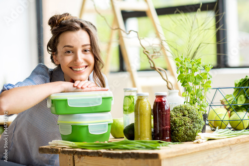Fotografía Portrait of a young smiling woman with green lunch boxes indoors