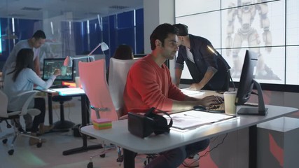  Young creative computer game designer working with colleagues in dark office.