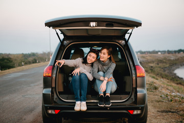 Two happy Asia woman friends enjoying road trip in hatchback car,flare light

