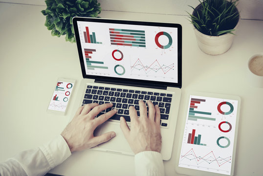 hands writing on a laptop with tablet and phone finances graphics