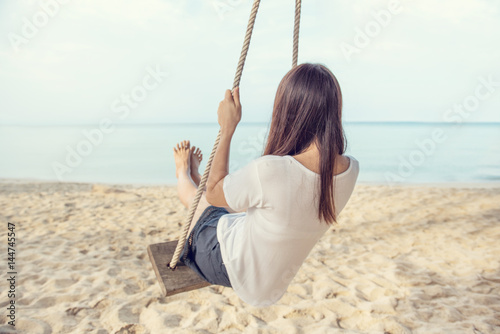 Fototapeta Młoda kobieta relaksuje na huśtawkach w plaży, tylny widok, wolności lato.