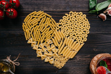 Dried pasta in heart shape top view. Pasta and vegetables on the dark wooden table