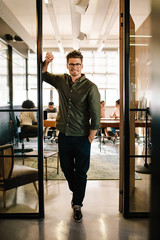 Happy young businessman standing in office doorway