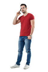 Wall Mural - Confident young handsome man on the mobile phone looking at camera. Full body length portrait isolated over white studio background.