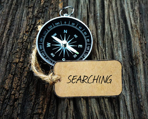 Wall Mural - Compass and paper tag written with SEARCHING on wooden background.