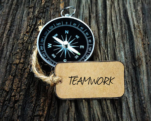 Wall Mural - Compass and paper tag written with TEAMWORK on wooden background.