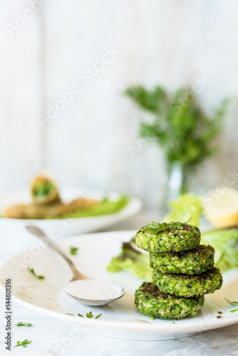 Fotografía falafel verdi e salsa tahini su piatto bianco; erbe aromatiche e involtini farci