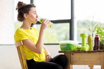 Wall Mural - Young sports woman in yellow t-shirt drinking water with mint and cucumber. Detox concept