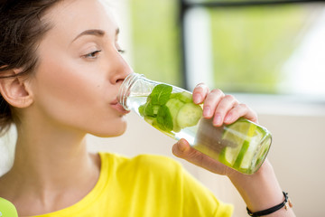 Wall Mural - Close-up of a woman drinking water with mint, cucumber and lime during a workout with dumbbells. Detox dieting concept