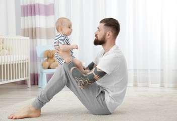 Canvas Print - Handsome tattooed young man playing with cute little baby at home