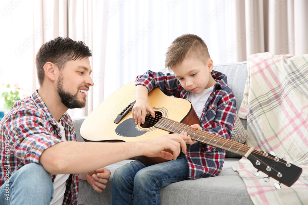 Father teaching his son to play guitar at home