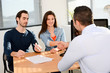 © W PRODUCTION - hand shaking and buying agreement contract signature between a young couple and a professional finance business man in office