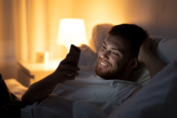 happy young man with smartphone in bed at night