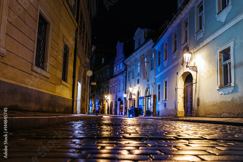 Fotomural Illuminated cobbled street with light reflections on the pavement in old histori