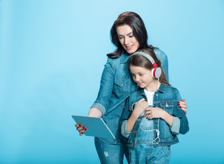 Wall Mural - happy mother and daughter in headphones using digital tablet in studio on blue