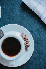 Wall Mural - From above view of white cup with coffee and roasted beans on saucer. 