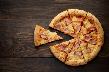 Wall Mural - Sliced hawaiian pizza with pineapple and ham on dark rustic wooden background.