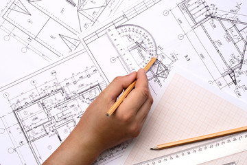 Man architect draws a plan , schedule , design , geometric shapes with a pencil and transparent protractor. On the desktop , on the graph paper  is a transparent ruler and pencil