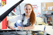 Young female mechanic working on car engine