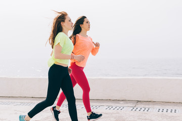 Two slim girls in sportswear running on the beach in the morning