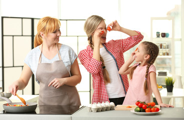 Wall Mural - Young woman with mother and daughter cooking in kitchen