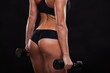 © satyrenko - Booty of attractive athletic woman holding dumbbells, back view isolated on dark background with copyspace