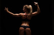 © satyrenko - Beautiful athletic woman in sporty cloths is posing, holding hands up and showing her perfect body, back view isolated on dark background with copyspace