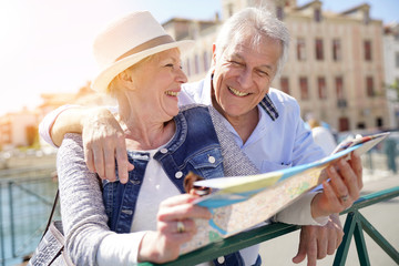 senior couple of tourists looking at city map