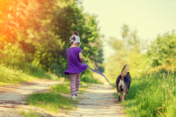 Wall Mural - Happy little girl with dog on a leash running on the dirt road outdoor back to camera