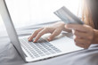 © oatawa - Close up hand using laptop and holding credit card on the bed, Online shopping easy.