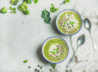 Spring broccoli green cream soup with mint and coconut cream in bowls over light grey marble background, top view, copy space. Clean eating, dieting, vegan, vegetarian, healthy food concept