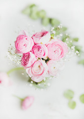 Wall Mural - Light pink spring ranunkulus flowers bouquet on white marble background, top view, selective focus, copy space, vertical composition. Spring greeting card concept