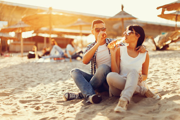 Wall Mural - Happy young couple drinking beer and having fun at the beach during sunset