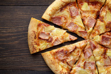 Sliced Hawaiian Pizza With Ham And Pineapple On Dark Wooden Table.