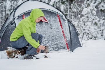 happy woman cooking near winter tent camp in the snow forest.