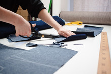 Hands Of Seamstress Cutting A Jeans Fabric With Scissors On White Table