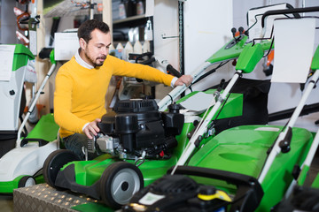 Wall Mural - young guy deciding on best lawnmower in garden equipment shop